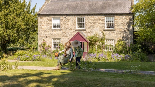 Two people, one a wheelchair user, admiring flowers in front of a stone-built house